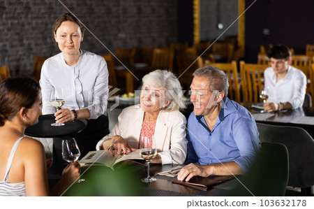 Waitress serves glass of wine and helps adult family of three decide to choose snack on menu 103632178