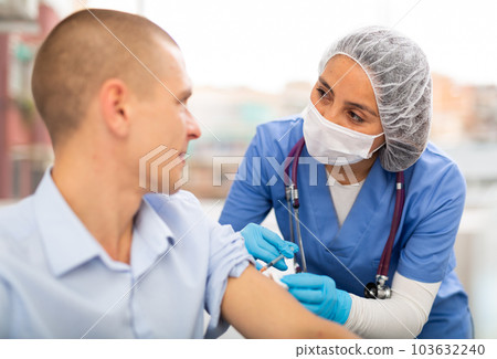 Doctor in a protective mask injects a vaccine to a man with syringe 103632240