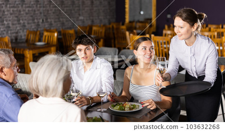 Friendly waitress brought glass of wine for elderly couple and young married spouses Friendly waitress brought glass of wine for elderly couple and young married spouses 103632268