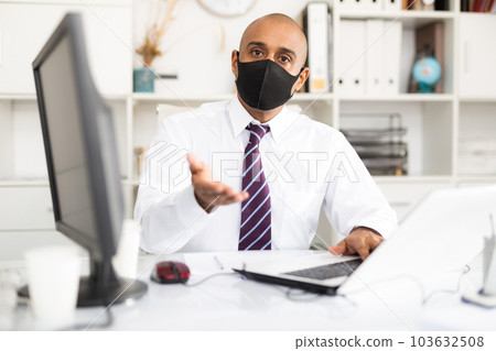 Latin manager in office at computer working in protective medical mask.Isolation during quarantine 103632508