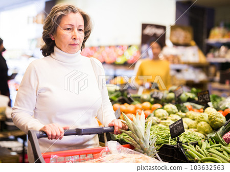 Elderly woman walking with shopping trolley in grocery shop 103632563