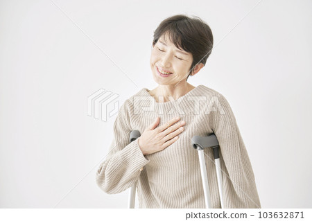 A middle-aged woman holding a crutch and stroking her chest White background 103632871