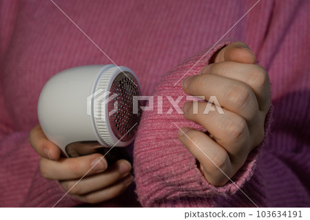 Woman using Anti-pilling razor at home. Device for shaving clothes. Anti-Plush fabric Shaver. Electric portable sweater pill defuzzer Lint remover from pink acrylic or wool sweater. Slow fashion Woman using Anti-pilling razor at home. Device for shaving clothes. Anti-Plush fabric Shaver. Electric portable sweater pill defuzzer Lint remover from pink acrylic or wool sweater. Slow fashion 103634191
