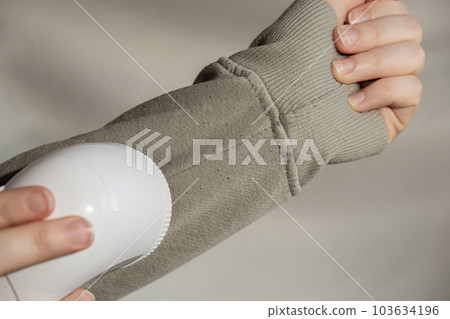 Woman using Anti-pilling razor at home. Device for shaving pellets clothes. Anti-Plush fabric Shaver. Electric portable sweater pill defuzzer Lint remover from acrylic or wool sweater. Sustainability Woman using Anti-pilling razor at home. Device for shaving pellets clothes. Anti-Plush fabric Shaver. Electric portable sweater pill defuzzer Lint remover from acrylic or wool sweater. Sustainability 103634196
