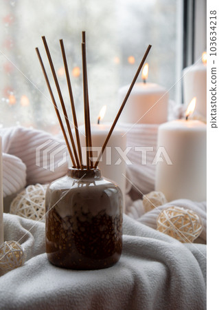 Aroma reed diffuser. Bottle container with wood stick diffusers Essential oils to scent your home fragnance concept autumn holidays at cozy home on the windowsill Hygge aesthetic atmosphere on knitted 103634218
