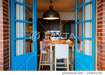 Little smiling child sitting at table having breakfast .Kid have a meal home. Caucasian happy preschool girl with croissant. Family lunch or dinner time. 103641785