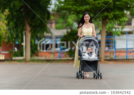 happy mother pushing infant baby stroller and walking in park happy mother pushing infant baby stroller and walking in park 103642542