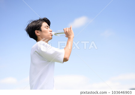 A young man drinking water in a plastic bottle 103646903