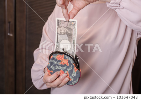 [一位家庭主婦從釦子裡拿出一張 10,000 日元的鈔票] 103647048
