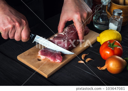 Chef cutting beef meat with knife on kitchen, cooking food. Vegetables and spices on kitchen table to prepare delicious lunch 103647081