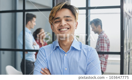 Portrait of a confident young businessman posing with his arms crossed in an office with his colleagues in the background. 103647775