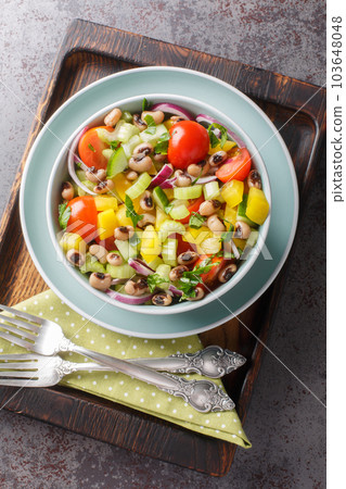Salad with tomatoes, celery, cucumber, onion, pepper and boiled black-eyed peas close-up in a bowl. Vertical top view 103648048