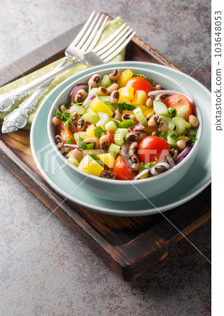 Fresh salad with cherry tomatoes, celery, yellow pepper, black-eyed peas, cucumber and onion close-up in a bowl. Vertical 103648053