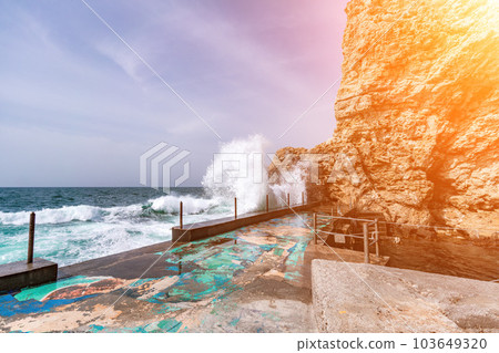 woman sea travel. A woman in a blue jacket stands on a rock above a cliff above the sea, looking at the stormy ocean. Girl traveler rests, thinks, dreams, enjoys nature 103649320