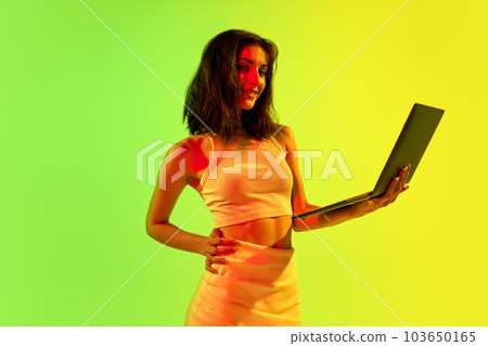Image with charming girl, freelancer holding laptop and working over acid gradient background. Remote work, online, sales Image with charming girl, freelancer holding laptop and working over acid gradient background. Remote work, online, sales 103650165