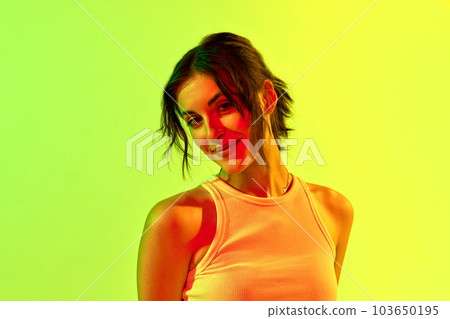 Portrait of charming girl, teenage, student with short hair smiling and posing with joyful face over yellow background in neon light 103650195