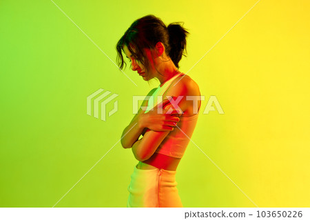 Portrait with one beautiful sad, upset girl with short hair standing alone and crying over acid green background in neon light. Spoiled mood 103650226