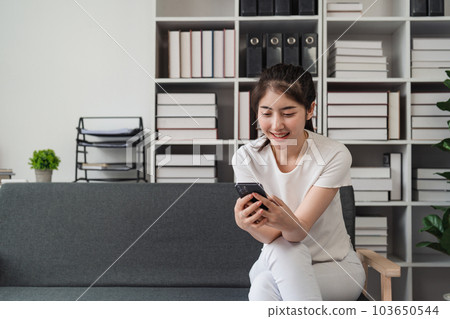 Young relaxed smiling pretty woman relaxing sitting on sofa at home. Female feeling joy enjoying with mobile phone on cozy couch Young relaxed smiling pretty woman relaxing sitting on sofa at home. Female feeling joy enjoying with mobile phone on cozy couch 103650544