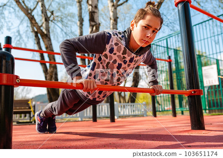 School physical education lessons. A caucasian teenage boy in a tracksuit is doing push-ups from the horizontal bar. Bottom view. Health and sport School physical education lessons. A caucasian teenage boy in a tracksuit is doing push-ups from the horizontal bar. Bottom view. Health and sport 103651174