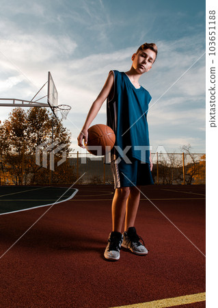Sports and basketball. A young teenager in a black tracksuit poses with a basketball on the Playground. Vertical Sports and basketball. A young teenager in a black tracksuit poses with a basketball on the Playground. Vertical 103651188