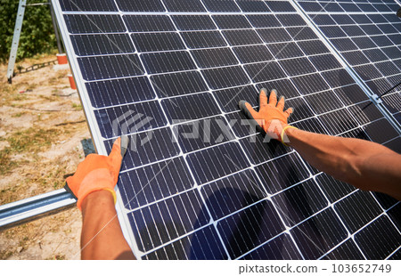 Close up of man solar technician mounting solar modules for generating electricity through photovoltaic effect. Male hands in work gloves assembling photovoltaic solar panels. Close up of man solar technician mounting solar modules for generating electricity through photovoltaic effect. Male hands in work gloves assembling photovoltaic solar panels. 103652749