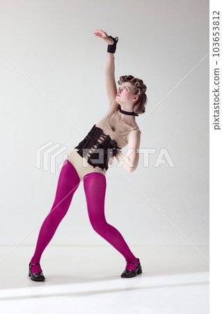 Extraordinary look. Portrait of pretty young girl in black corset and pink tights with blushing cheeks posing against grey studio background 103653812