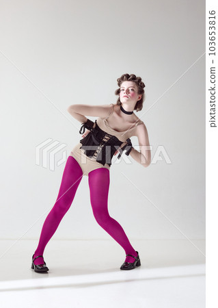 Portrait of young beautiful girl with blushing cheeks, wearing in black corset and pink tights, posing against grey studio background Portrait of young beautiful girl with blushing cheeks, wearing in black corset and pink tights, posing against grey studio background 103653816