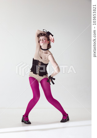 Extraordinary look. Portrait of pretty young girl in black corset and pink tights with blushing cheeks posing against grey studio background 103653821