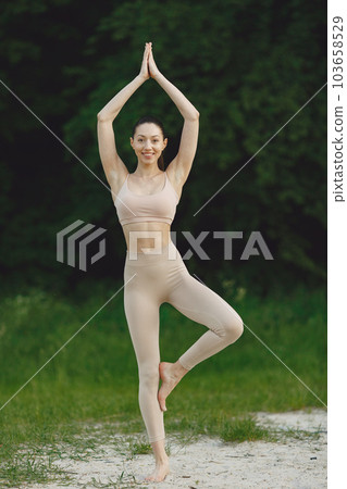 Pretty lady training on a summer beach. Brunette doing yoga. Girl in a sportsuit. 103658529