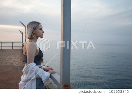 Blonde woman standing on pier and looking at horizon, sea and cloudy sky 103658845