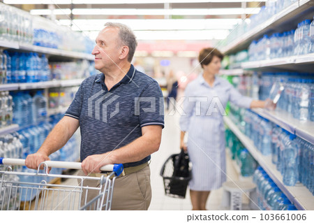 Mature man considering bottle of drinking water in alcoholic section of supermarket Mature man considering bottle of drinking water in alcoholic section of supermarket 103661006