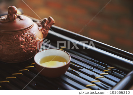 Clay teapot and a cup of hot green tea on a wooden tray Clay teapot and a cup of hot green tea on a wooden tray 103666210