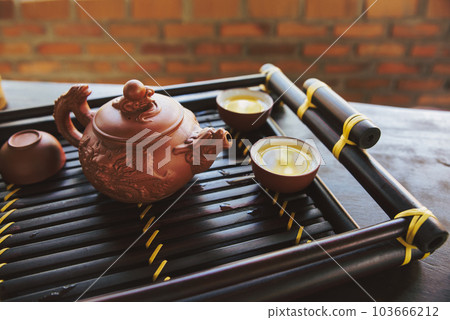 Clay teapot and a cup of hot green tea on a wooden tray Clay teapot and a cup of hot green tea on a wooden tray 103666212