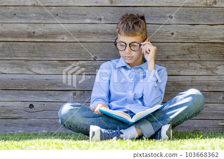 A boy reading a book on a grass 103668362