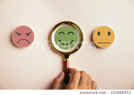 Magnifier in hand selected happy smiley face icon among emotions. Good feedback rating, customer review. Experience, satisfaction survey, mental health concept. Certificate demonstrates satisfaction. 103668452