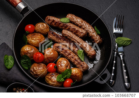 Delicious grilled sausages and potatoes in a sizzling frying pan 103668707