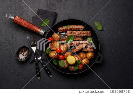 Delicious grilled sausages and potatoes in a sizzling frying pan 103668708