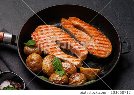 Grilled salmon steaks and potatoes in a frying pan Grilled salmon steaks and potatoes in a frying pan 103668712