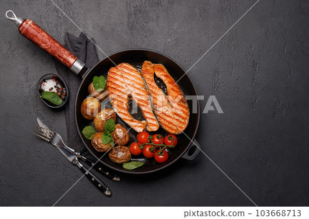 Grilled salmon steaks and potatoes sizzling in a frying pan Grilled salmon steaks and potatoes sizzling in a frying pan 103668713