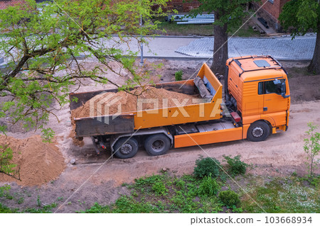 A large orange dump truck unloads the sand. A large orange dump truck unloads the sand. 103668934