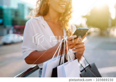 Stylish young woman shopping with phone on street. Woman is using mobile phone. Active lifestyle 103669150