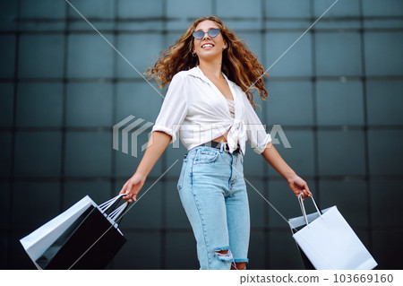 Young woman with shopping bags walking on street. Summer shopping. Sale, shopping, lifestyle concept 103669160