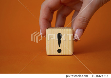 Exclamation mark symbol. Exclamation mark on wooden cubes. Businessman hand. Beautiful orange background. Business and Exclamation mark concept. Copy space. Exclamation mark symbol. Exclamation mark on wooden cubes. Businessman hand. Beautiful orange background. Business and Exclamation mark concept. Copy space. 103669984