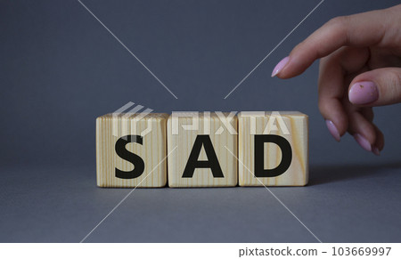 Sad symbol. Wooden cubes with words Sad. Businessman hand. Beautiful grey background. Business and Sad concept. Copy space. Sad symbol. Wooden cubes with words Sad. Businessman hand. Beautiful grey background. Business and Sad concept. Copy space. 103669997
