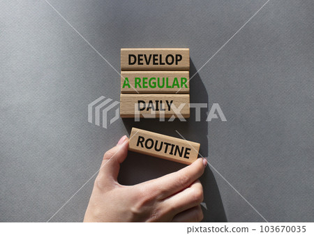 Develop a regular daily routine symbol. Concept words Develop a regular daily routine on wooden blocks. Beautiful grey background. Businessman hand. Business and concept. Copy space. 103670035