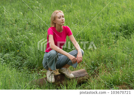 girl teenager squatting on a log in a meadow girl teenager squatting on a log in a meadow 103670721