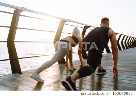 Romantic couple doing sport together at the beach pier. Two sporty athletes doing warming-up excersises. Romantic couple doing sport together at the beach pier. Two sporty athletes doing warming-up excersises. 103670993