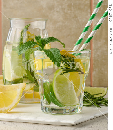 Lemonade in a transparent glass with lemon, lime, rosemary sprigs and mint leaves on a white background 103671088