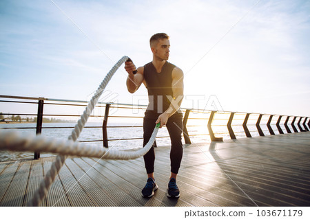 Young athlete wearing sports clothes is doing workout at the beach pier. Man doing exercises outdoors. Young athlete wearing sports clothes is doing workout at the beach pier. Man doing exercises outdoors. 103671179