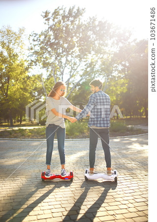 Young man and woman riding on the Hoverboard in the park. content technologies. a new movement. Young man and woman riding on the Hoverboard in the park. content technologies. a new movement. 103671486